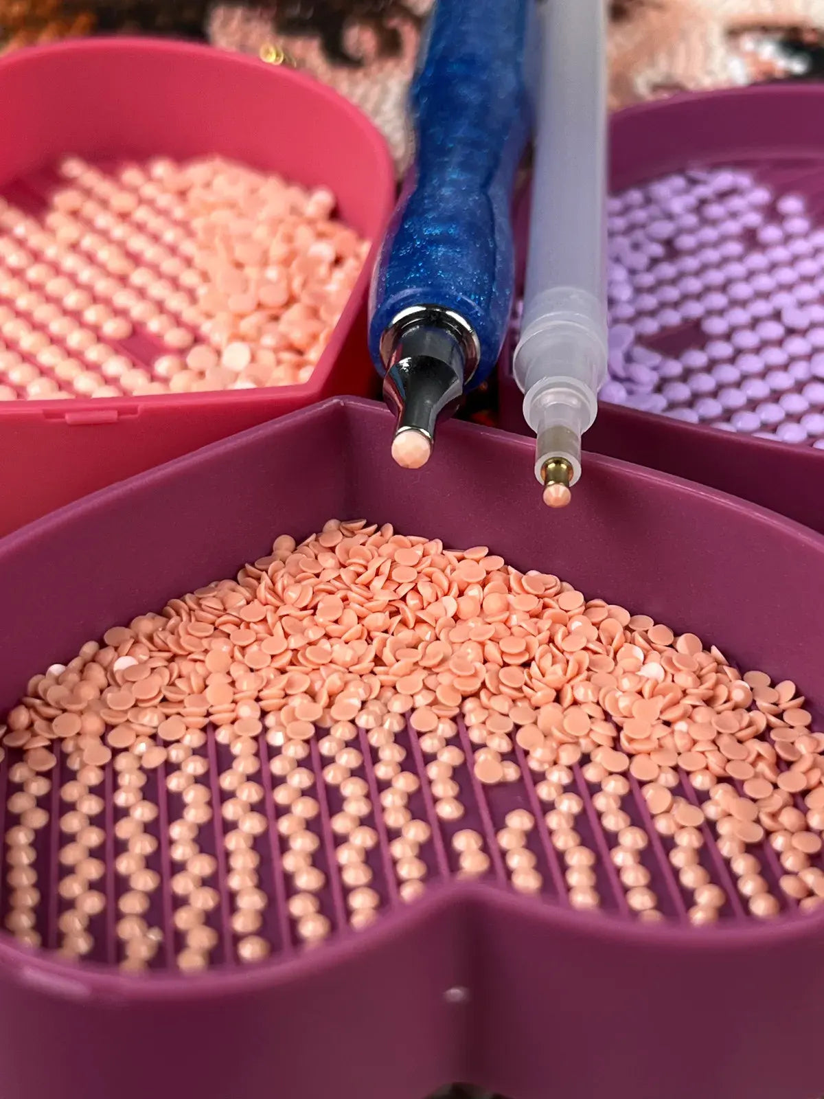 Close-up of diamond painting tools with peach and purple diamond beads in heart-shaped trays, including a blue drill pen and a precision applicator - FEELOOK Art