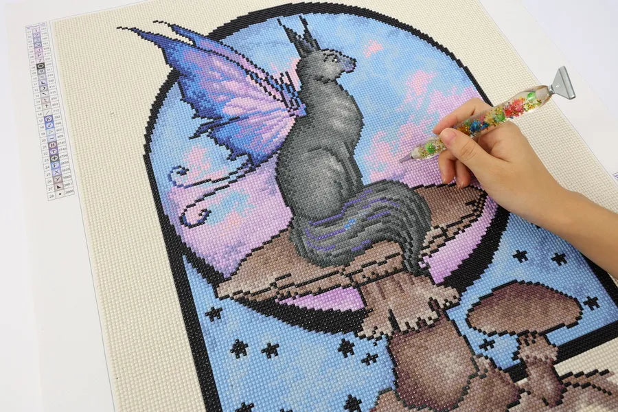 Close-up of Night Kitty diamond painting in progress, showing hand placing drills on a winged cat and mushroom scene under a pastel night sky - FEELOOK Art