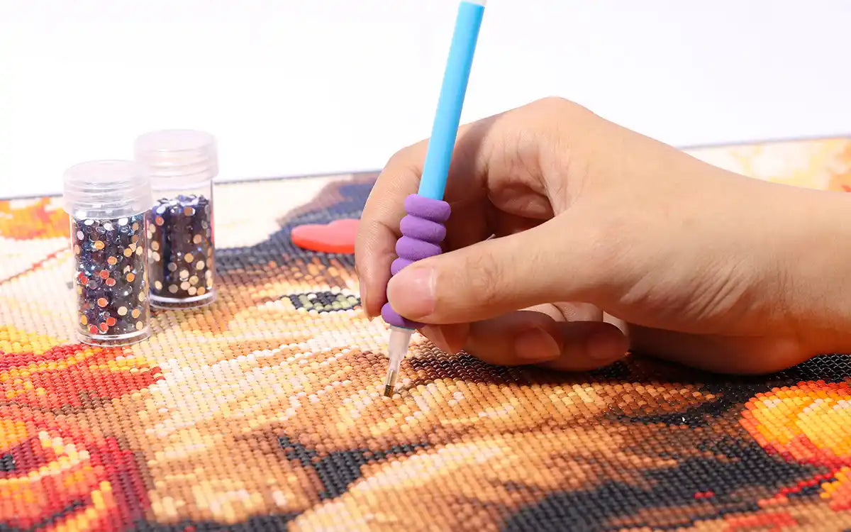 Close-up of a hand placing round diamond drills onto a sticky canvas with a stylus pen — detailed view of the diamond painting process